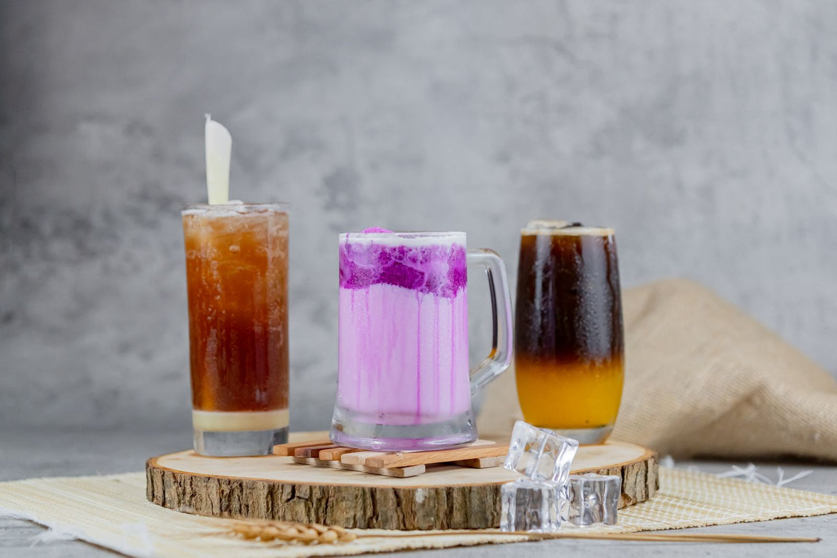 Assortiment de boissons healthy colorées : latte violet façon taro, café glacé et boisson rose, illustrant la diversité des tendances boissons 2026
