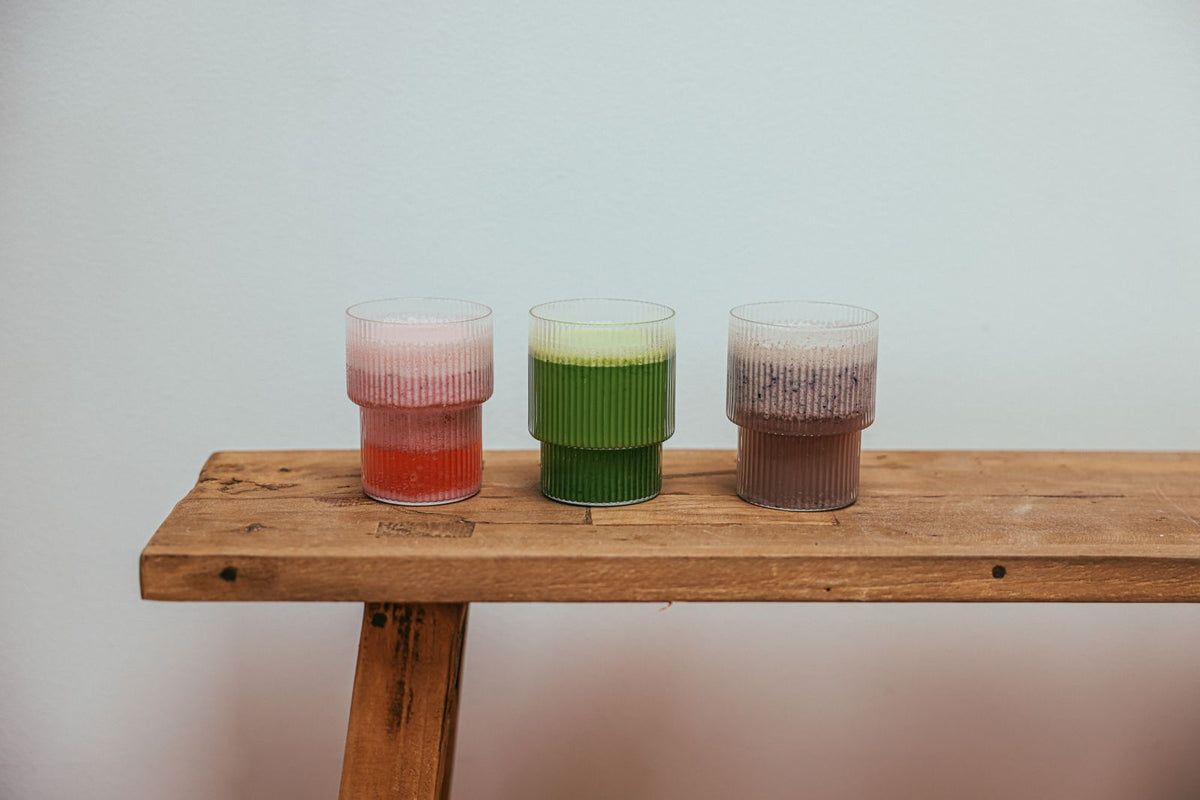 Trois boissons colorées variées, type bar à matcha, posées sur un comptoir en bois, illustrant une offre boissons diversifiée en studio
