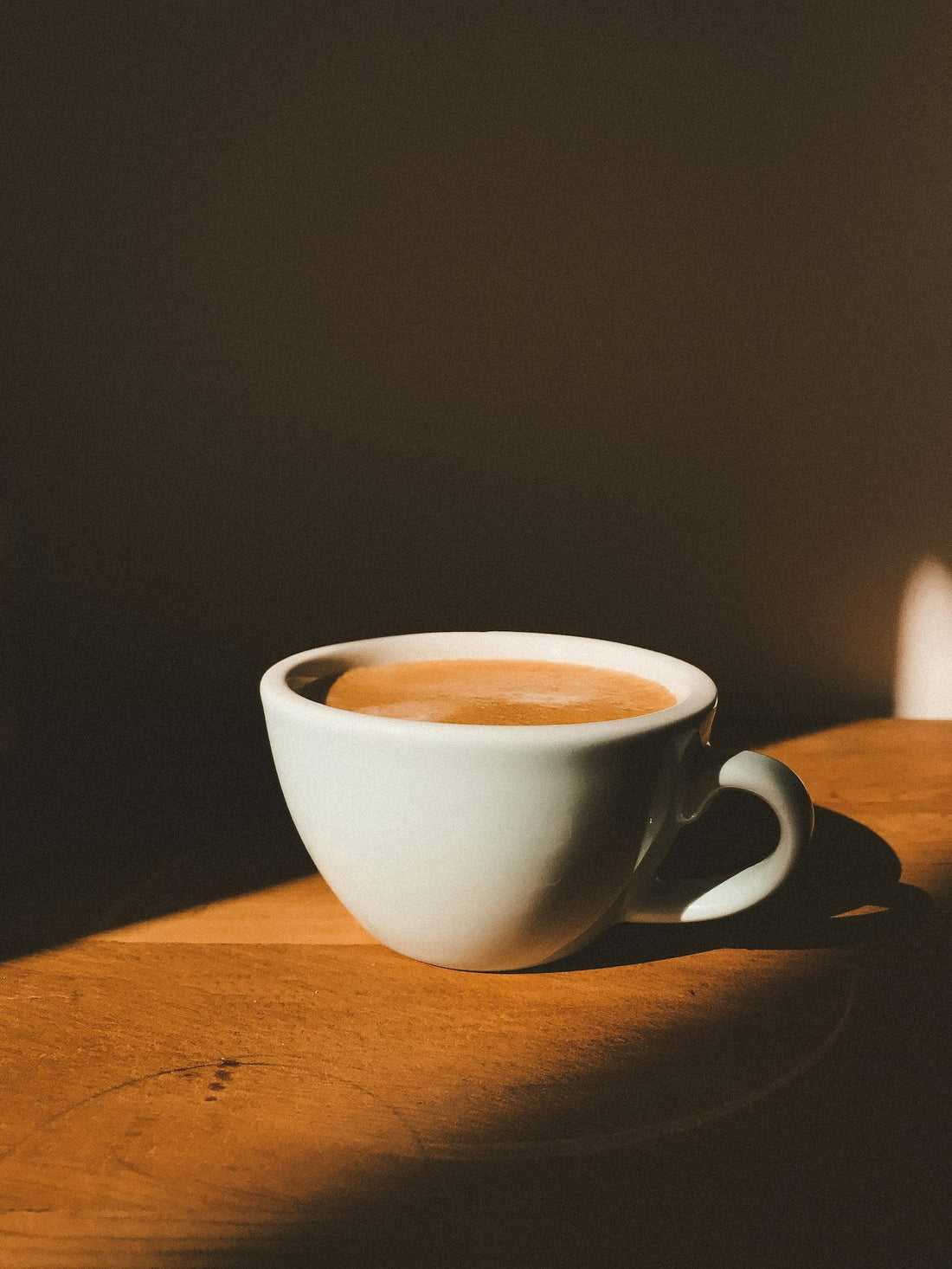 Tasse de café blanche posée sur une table en bois, lumière chaude et cosy