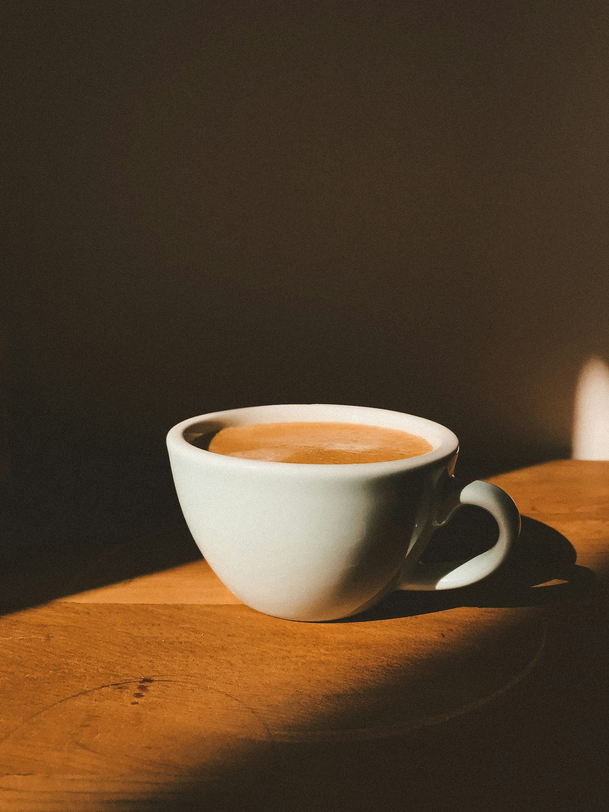 Tasse de café blanche posée sur une table en bois, lumière chaude et cosy