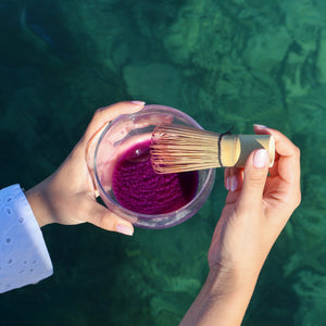 Fouet en bambou mélangeant la poudre d'ube Vytal Oya dans un bol de latte violet.