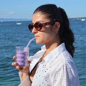 Personne dégustant un ube latte Vytal Oya en bord de mer au coucher du soleil.