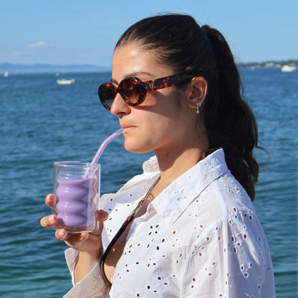 Personne dégustant un ube latte Vytal Oya en bord de mer au coucher du soleil.