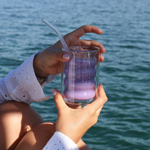 Ube latte Vytal Oya glacé tenu à la main avec vue sur la mer.